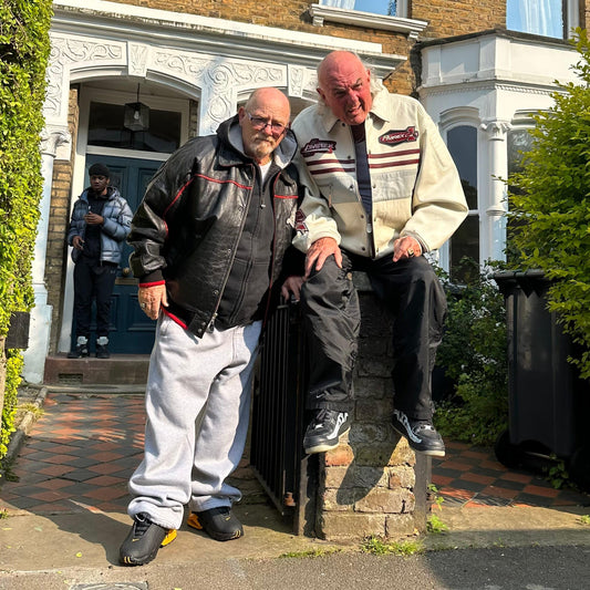 Two men wearing vintage sportswear jackets and trousers standing in front of a house.